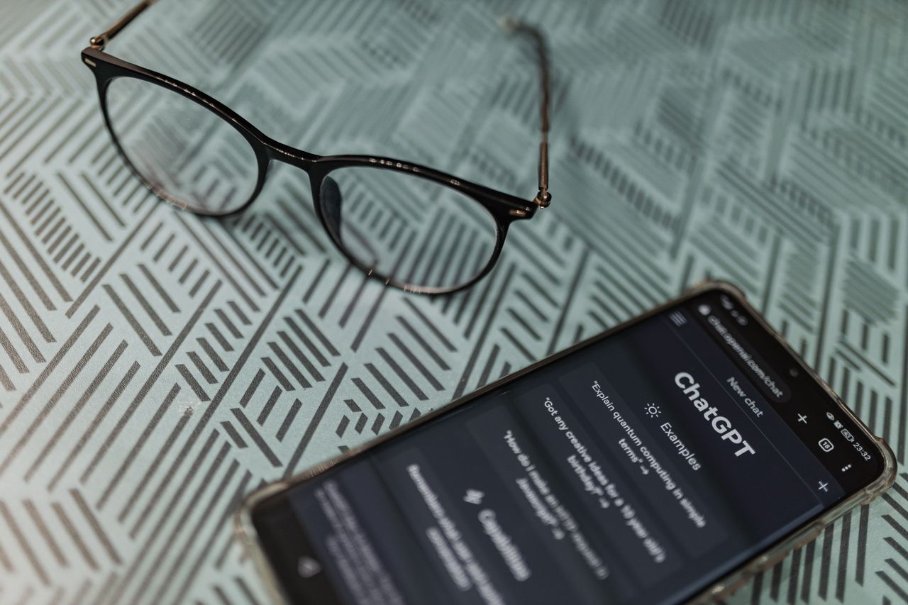 Mastering the First Impression: Your intriguing post title goes here Eyeglasses next to a smartphone displaying the ChatGPT AI app on a patterned surface.